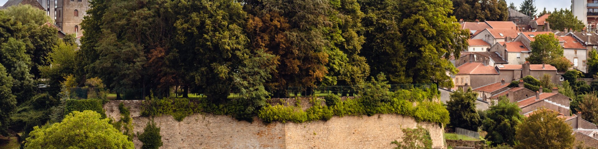 A historic town with a prominent church tower, lush greenery, and a stone wall.