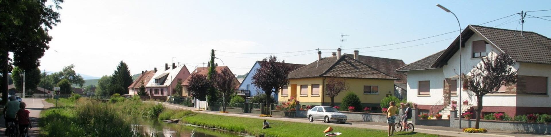 A canal with houses on one side and a road with pedestrians and cyclists on the other.