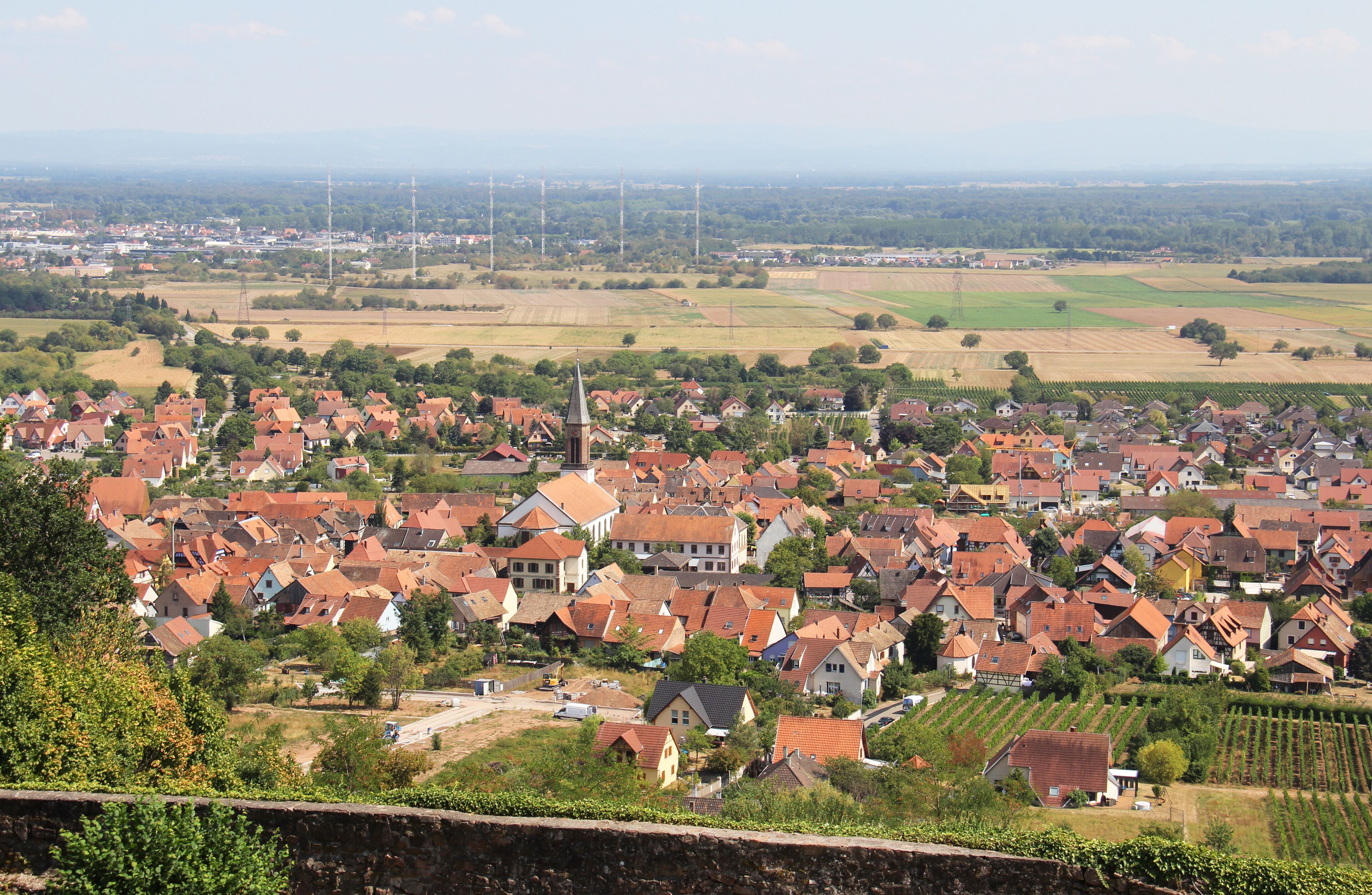 A town with red-roofed houses, a church, and wind turbines in the distance.