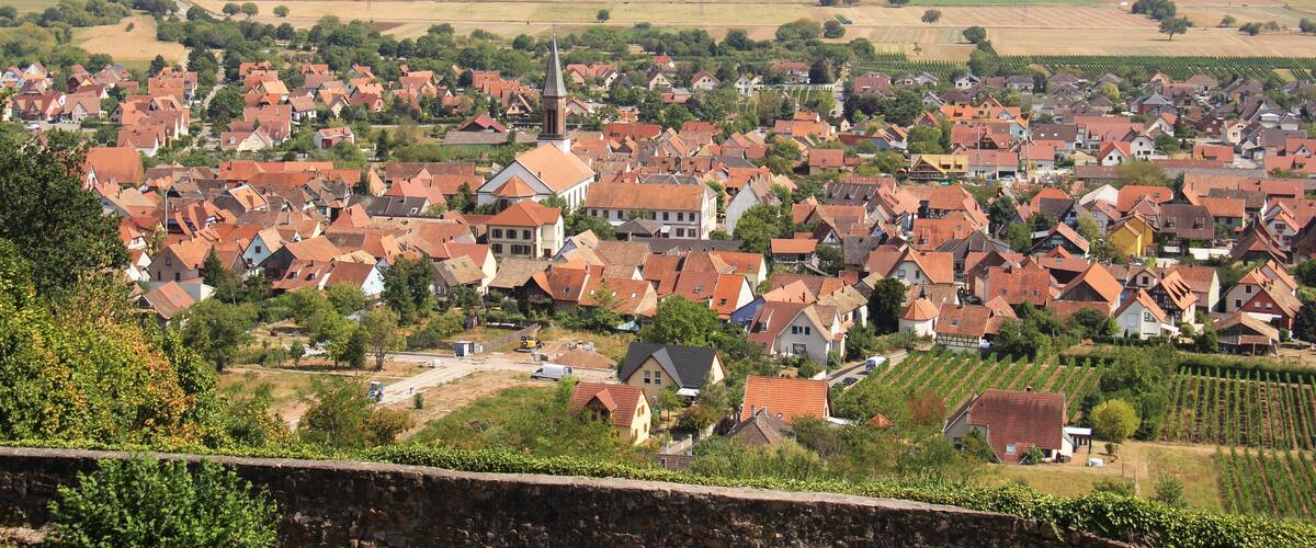 A town with red-roofed houses, a church, and wind turbines in the distance.