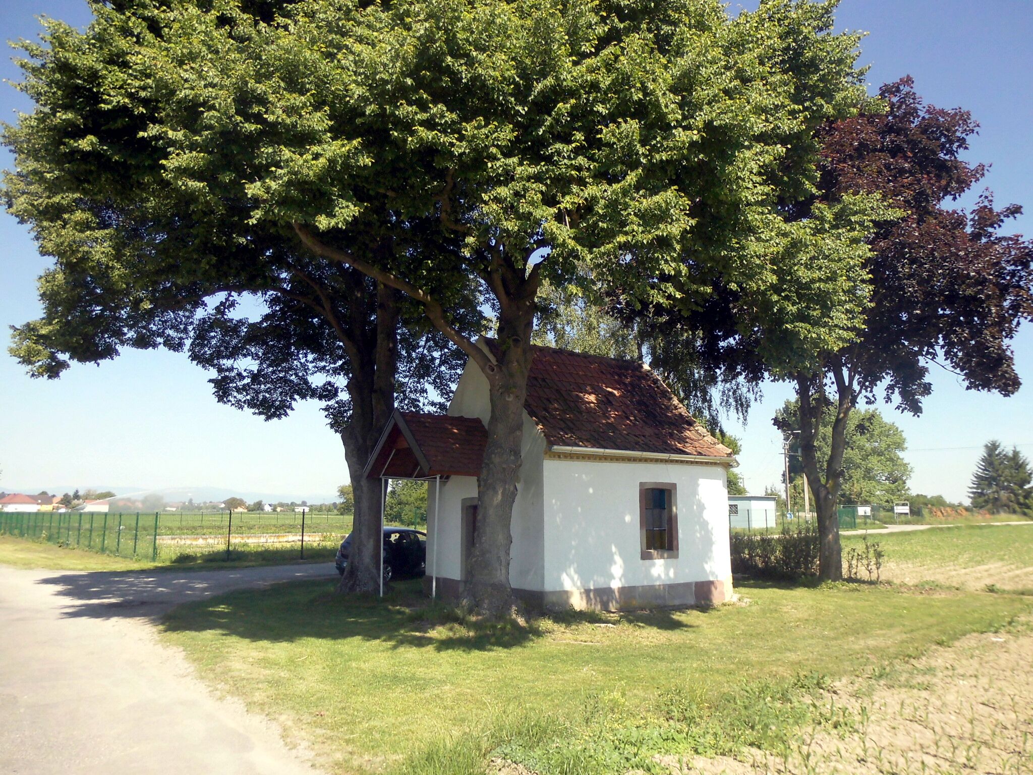 A small white building with a red roof, surrounded by lush green trees and a grassy field.