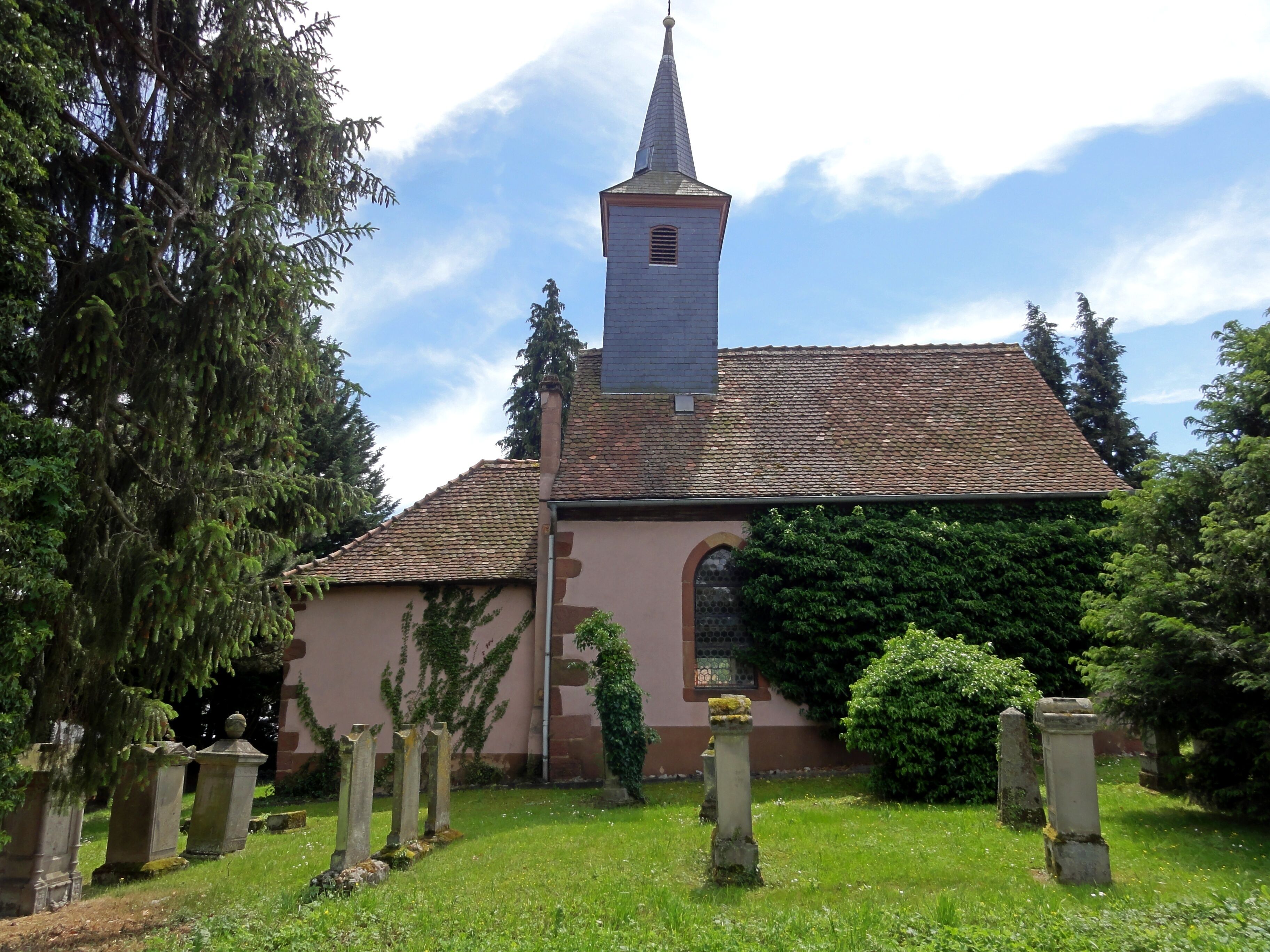 A church with a tall steeple and a tiled roof, surrounded by a cemetery with gravestones.