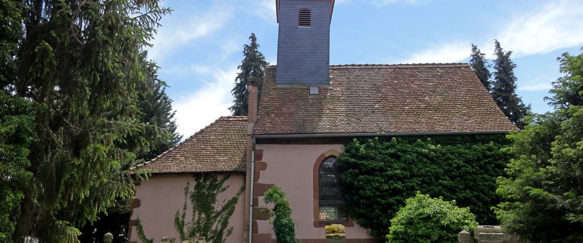 A church with a tall steeple and a tiled roof, surrounded by a cemetery with gravestones.