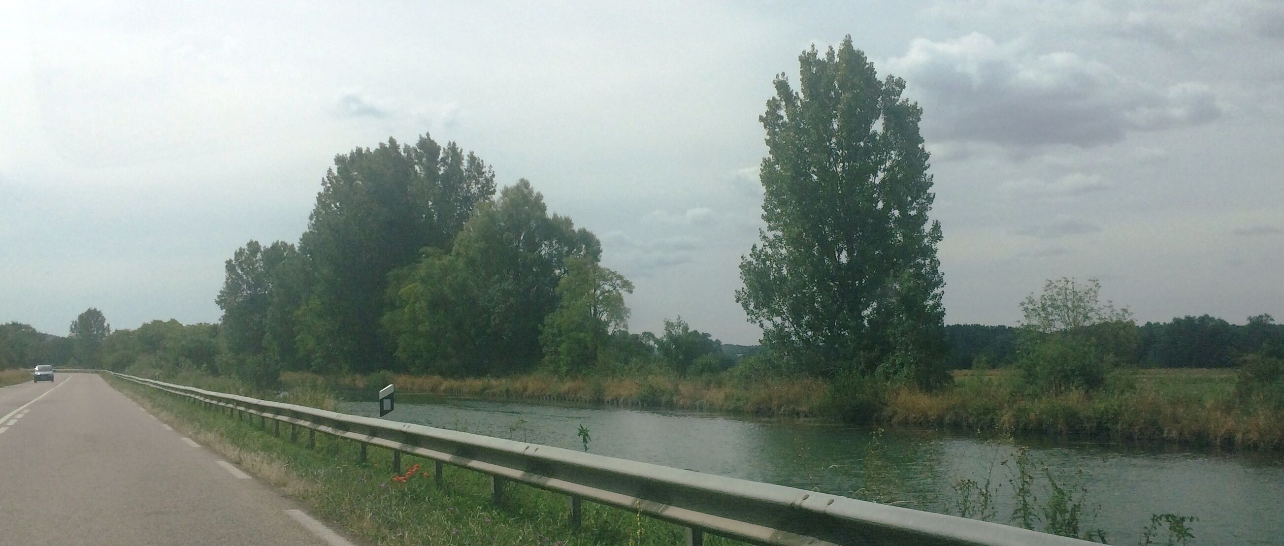A highway beside a river with trees and a cloudy sky.