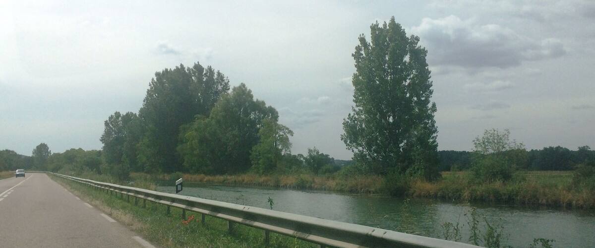 A highway beside a river with trees and a cloudy sky.
