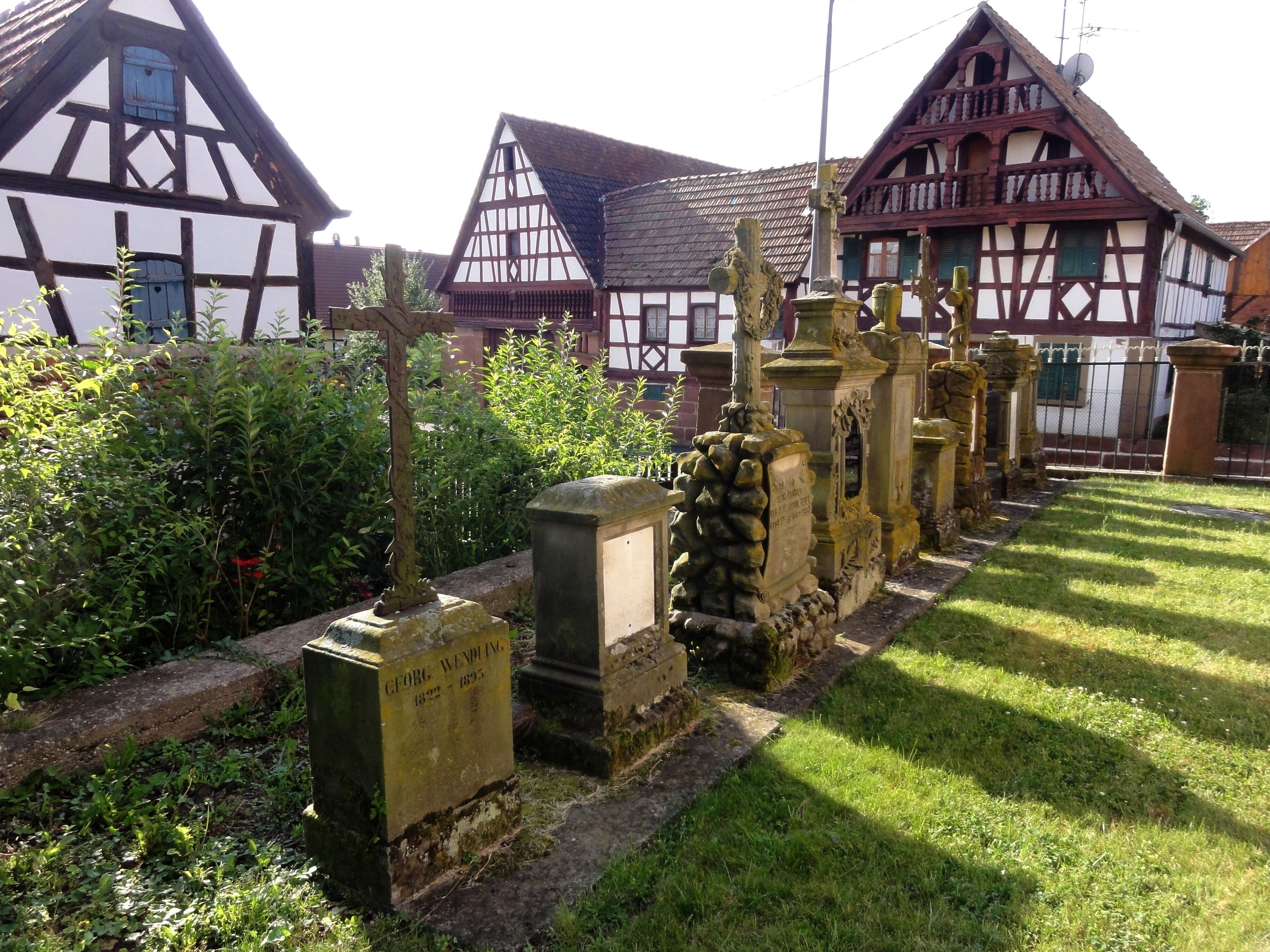 A cemetery with gravestones and traditional half-timbered houses in the background.