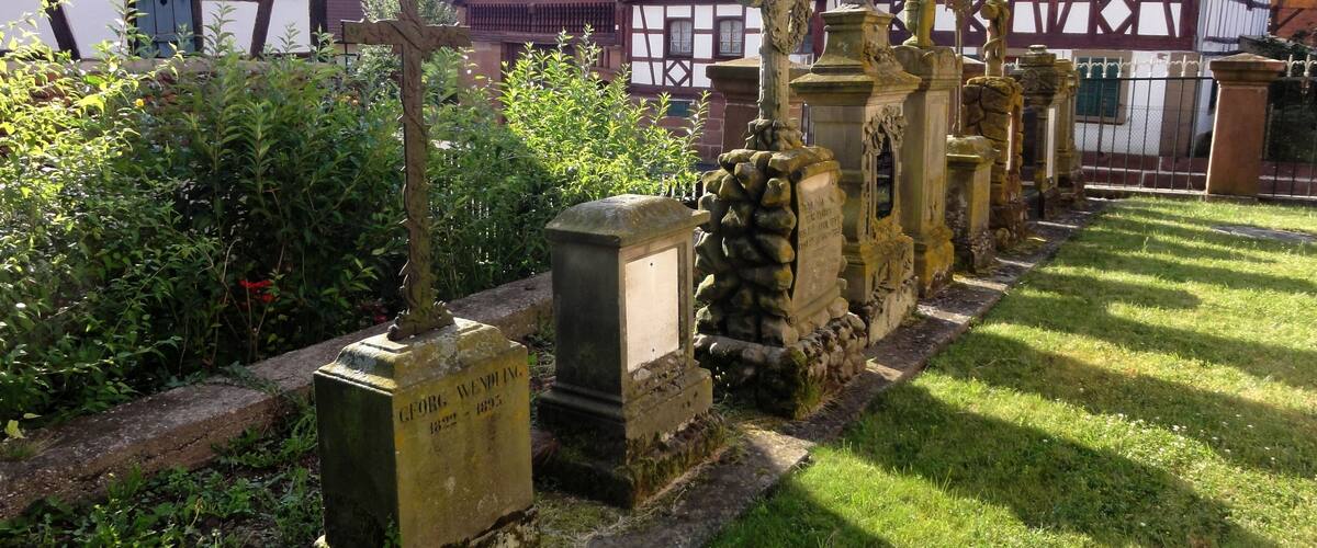 A cemetery with gravestones and traditional half-timbered houses in the background.