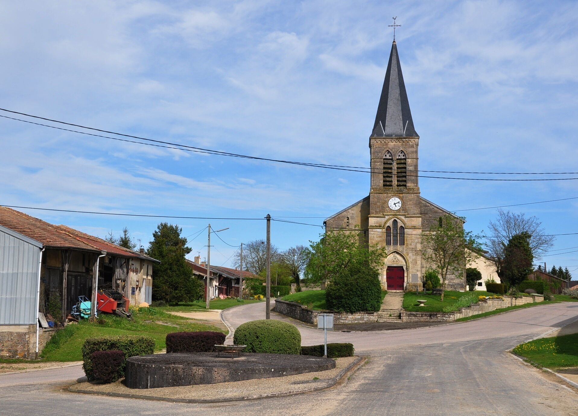 A church with a tall steeple and a clock, surrounded by a small village with houses and greenery.
