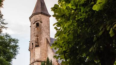 A church with a tall tower, surrounded by trees and a gravel path.