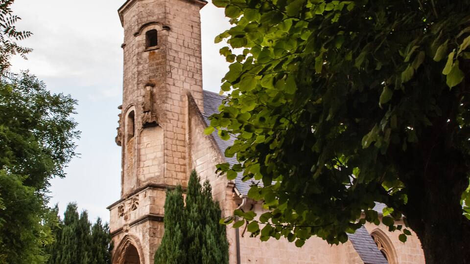 A church with a tall tower, surrounded by trees and a gravel path.