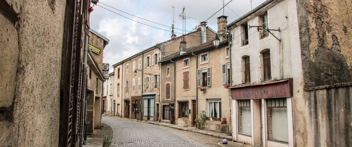 A cobblestone street lined with historic buildings, including a visible storefront with a sign that reads "DROGUERIA."