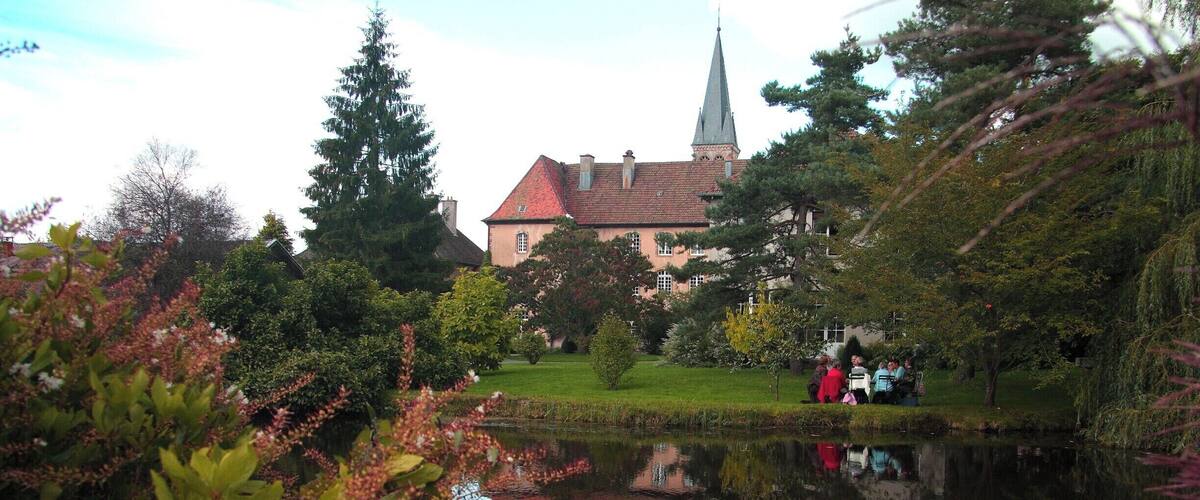 A serene pond with a church and a steeple in the background.