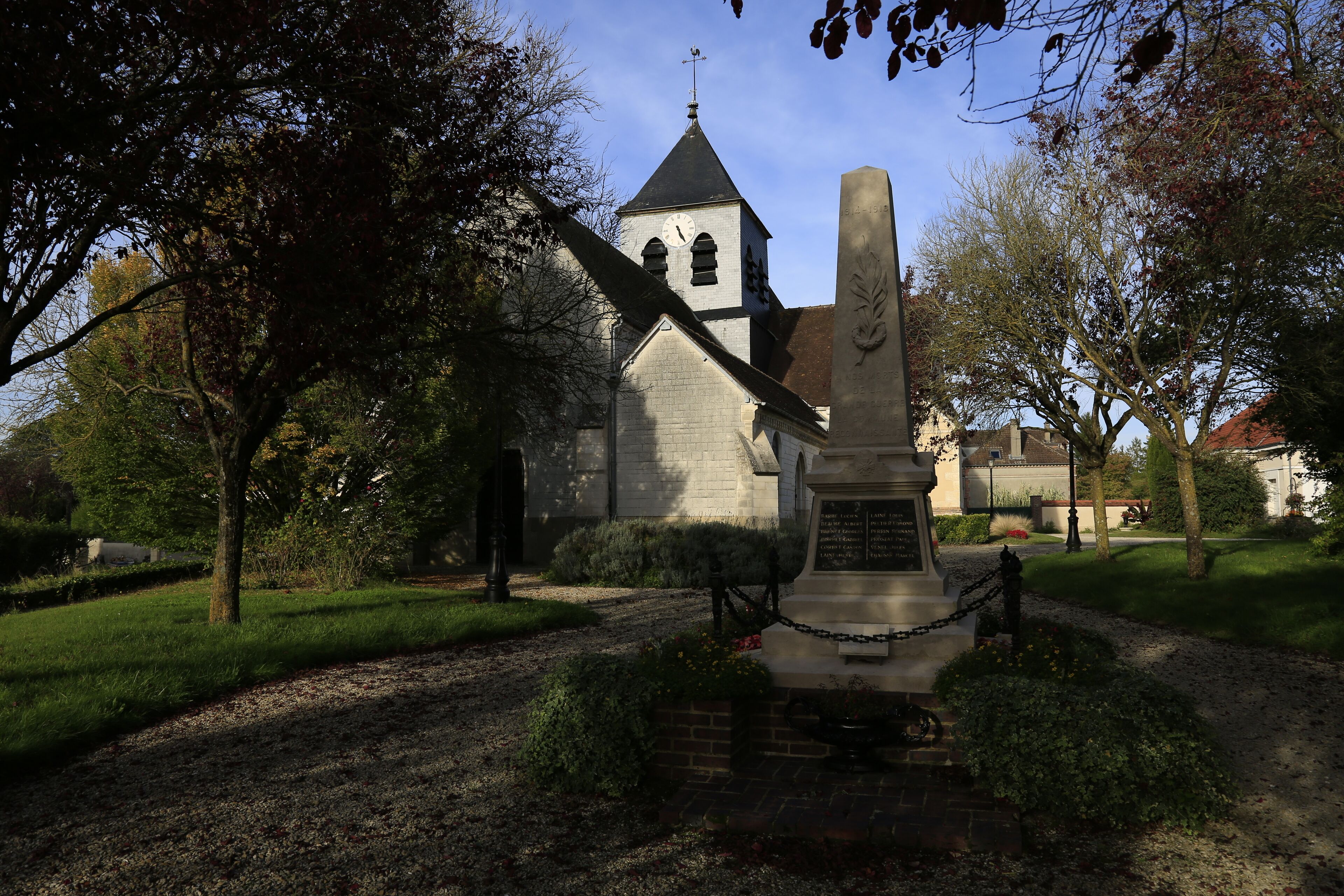 A church with a clock tower, surrounded by trees and a gravestone.
