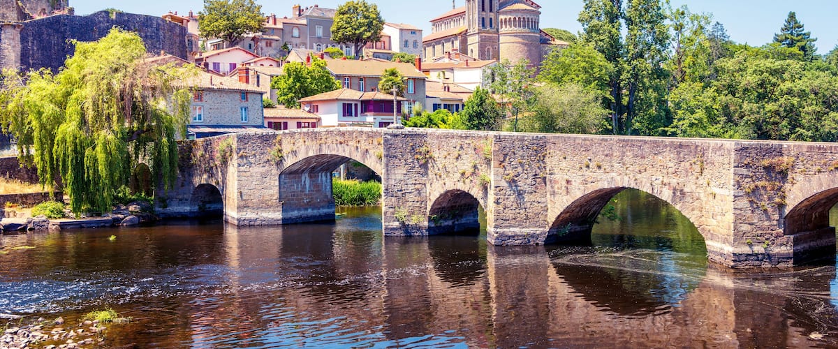 A stone bridge over a river with a town in the background, including a prominent church tower.
