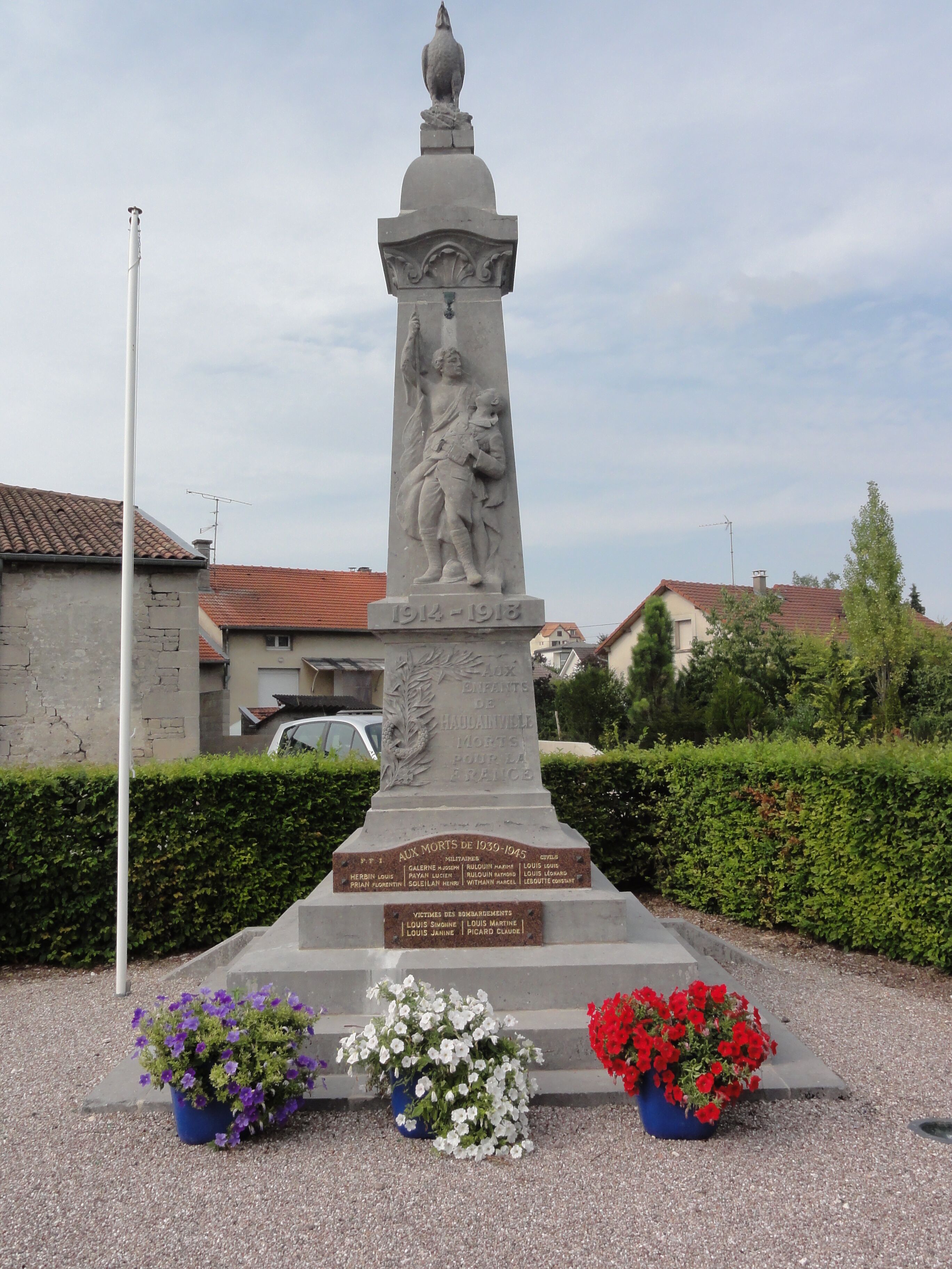 A monument with inscriptions and a statue, surrounded by greenery and residential buildings.