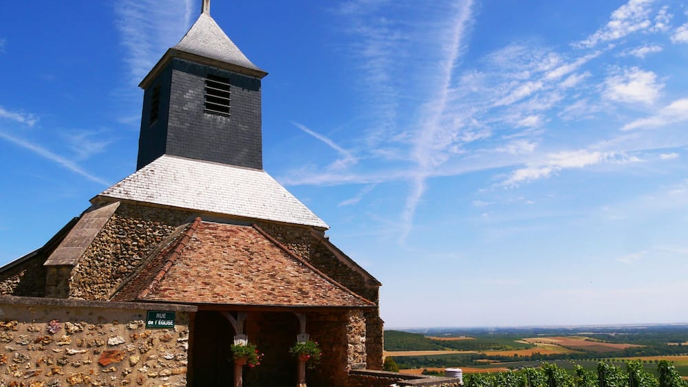 A stone church with a tall steeple and a tiled roof.