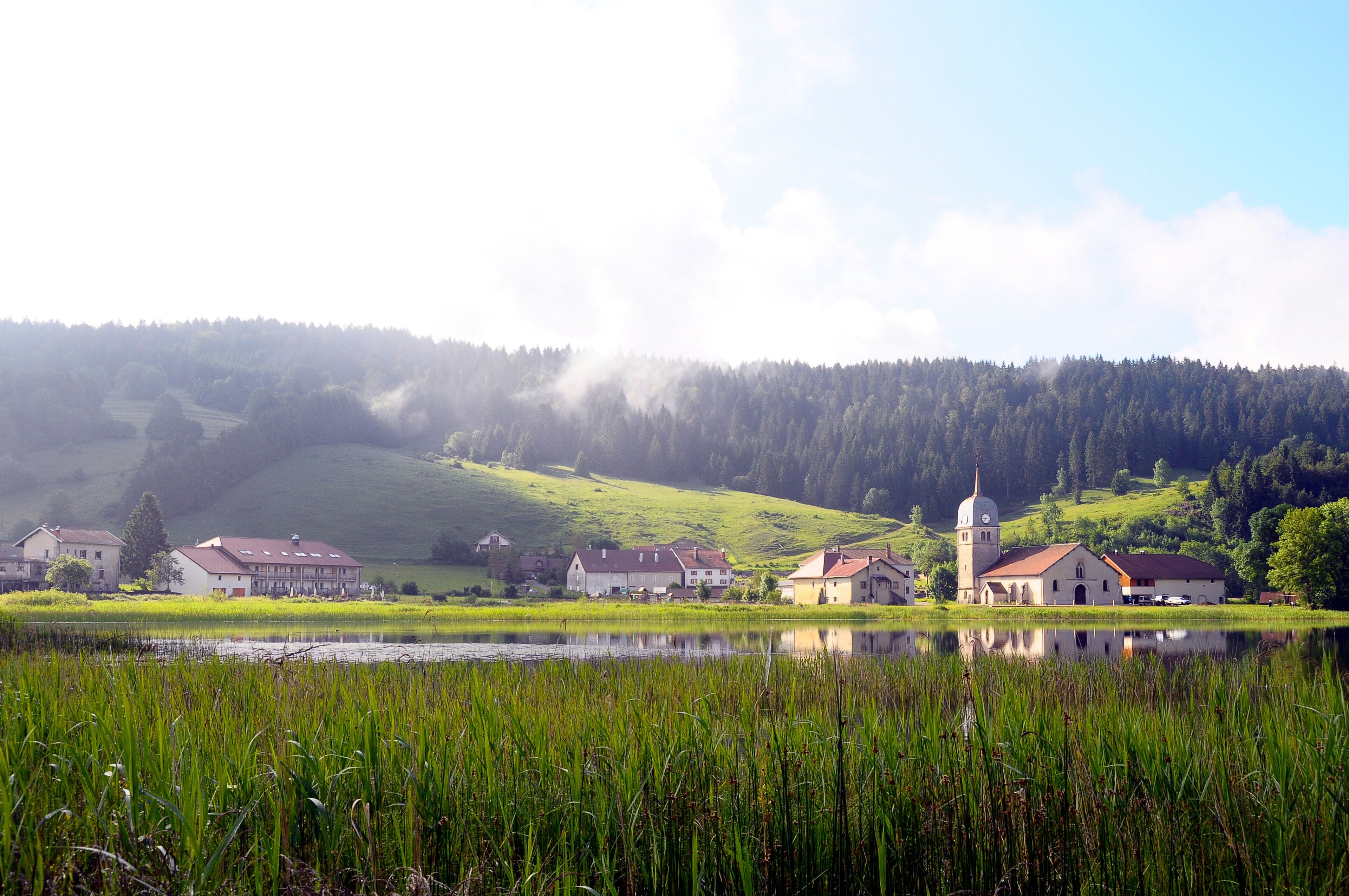 A serene lakeside village with houses and a church surrounded by lush greenery and hills.