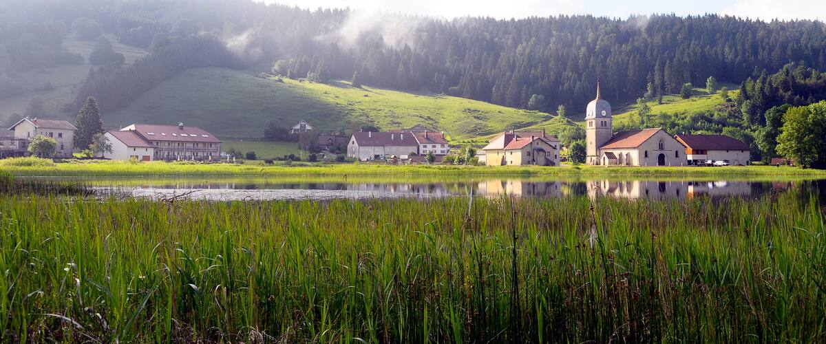 A serene lakeside village with houses and a church surrounded by lush greenery and hills.