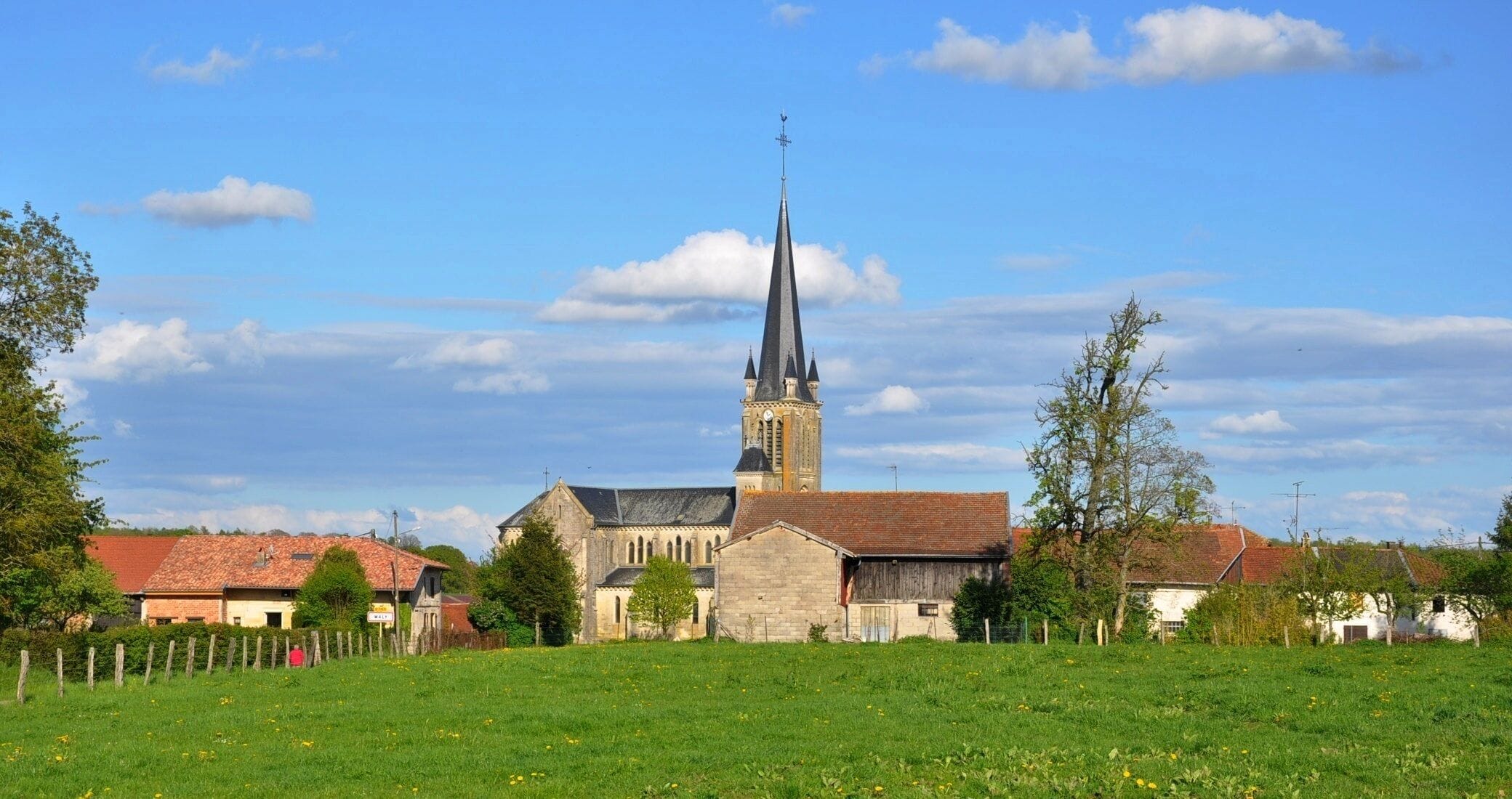 A church with a tall spire, surrounded by houses and a green field.