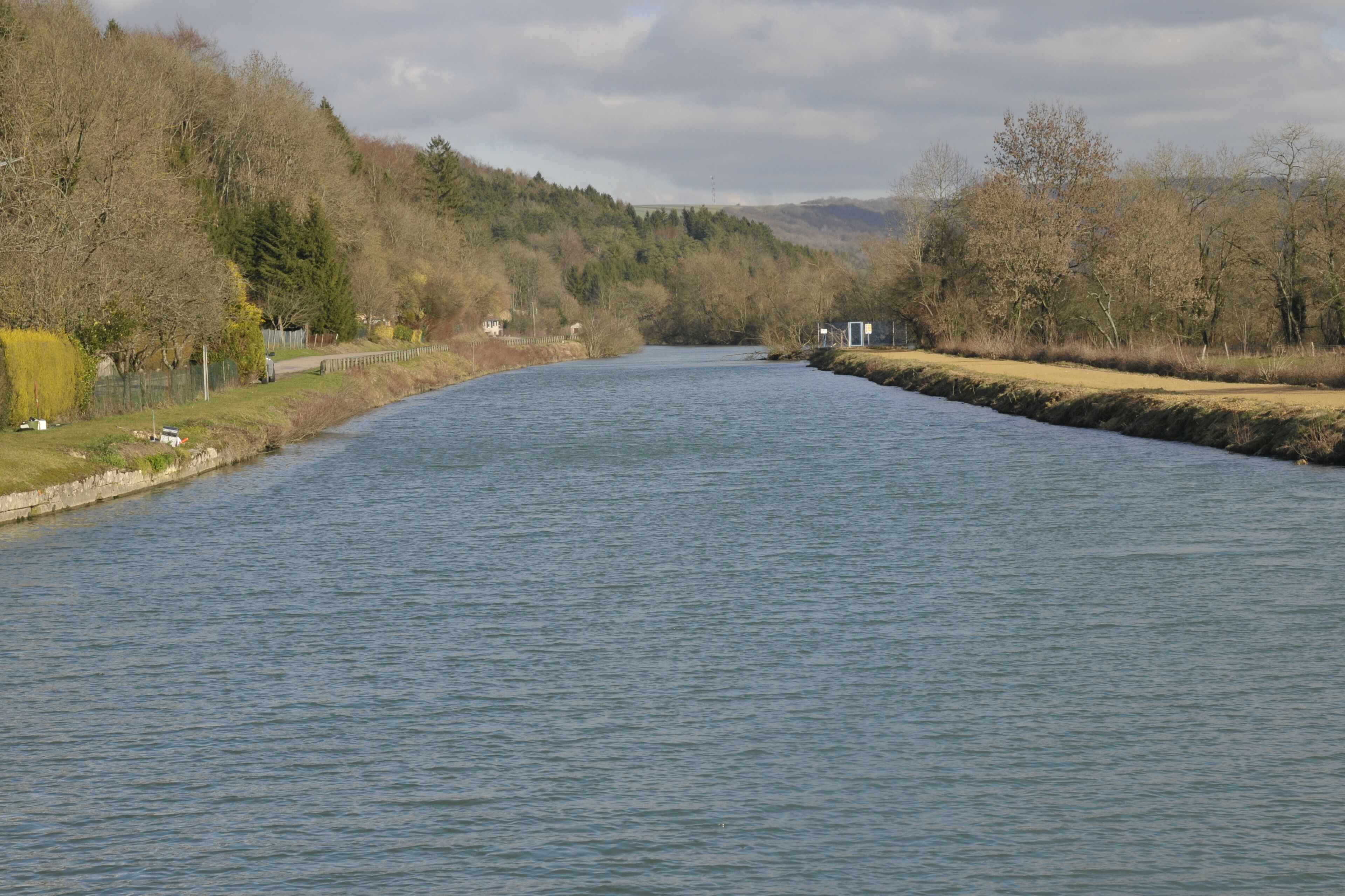A river flowing through a valley with trees and a small building on the left bank.