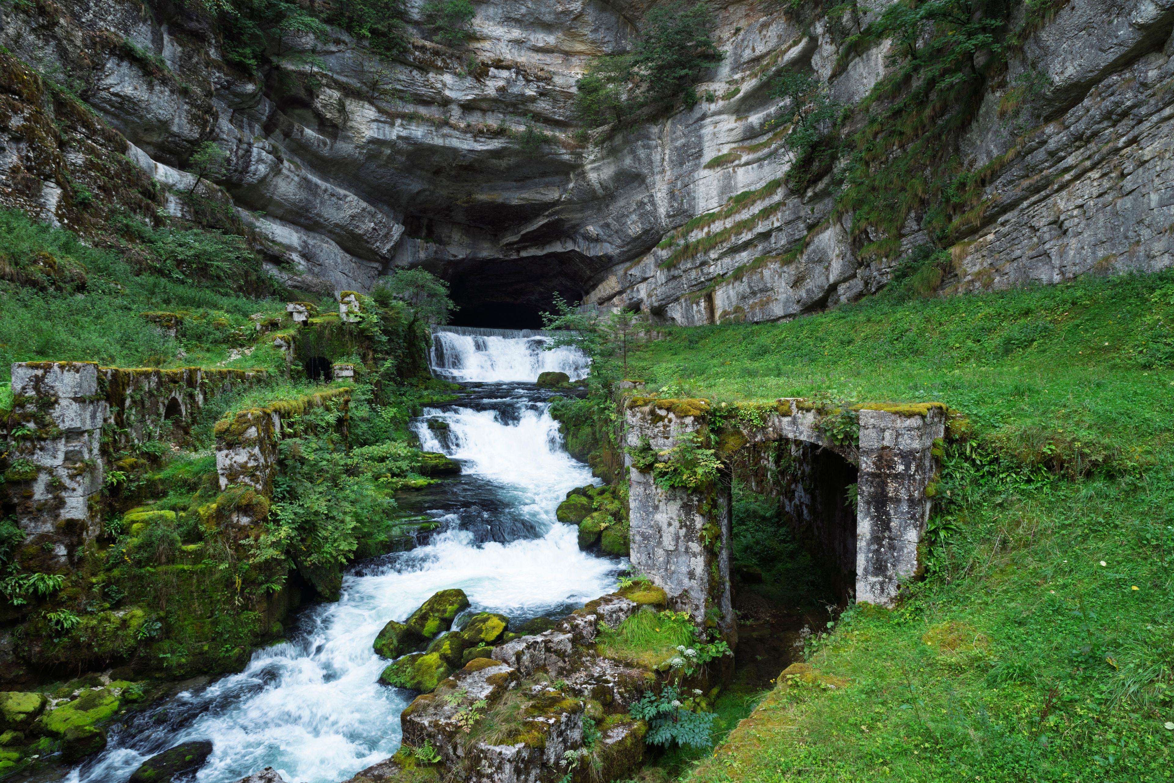 Une rivière qui traverse un défilé rocheux, bordé de structures en pierre recouvertes de mousse.