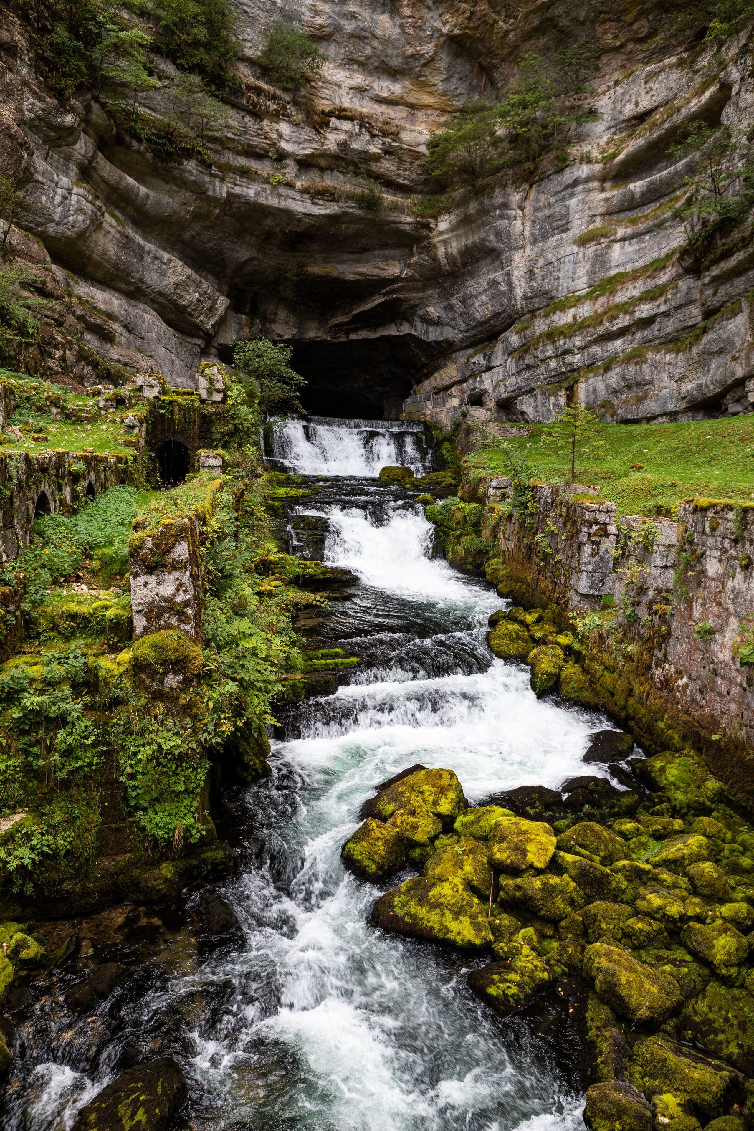 Une cascade d’eau se déversant dans un ravin rocheux, où les rochers et la végétation sont recouverts de mousse.