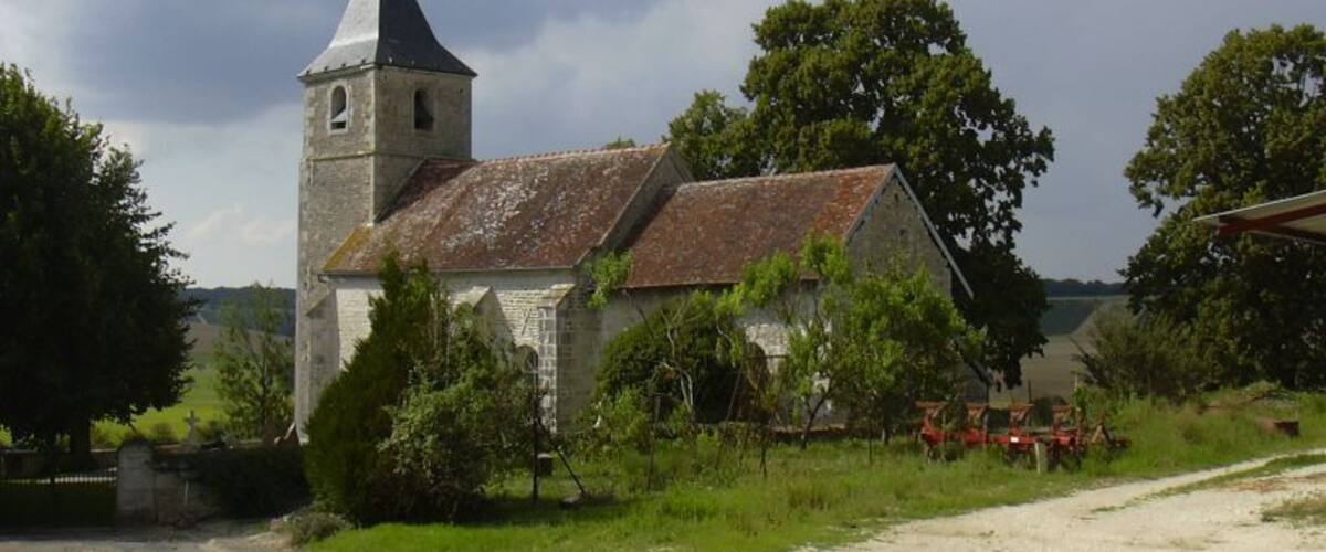 A church with a bell tower, surrounded by trees and a gravel path.