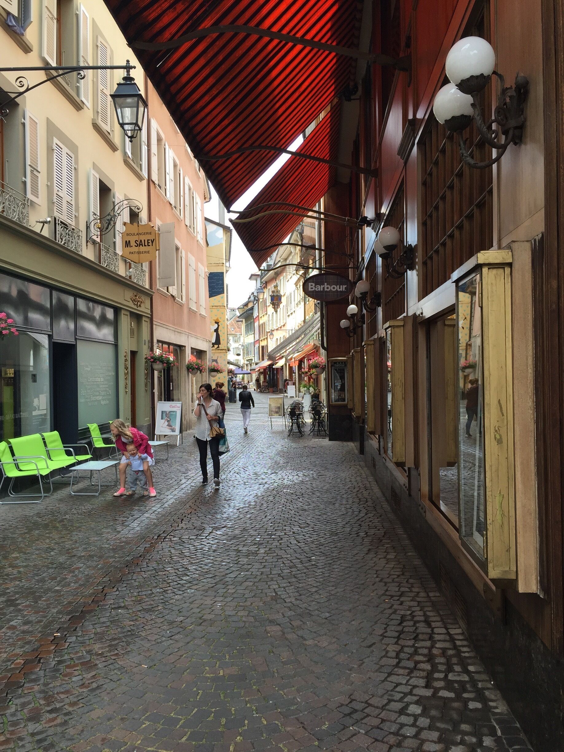 A cobblestone street with shops, a red awning, and hanging street lamps.