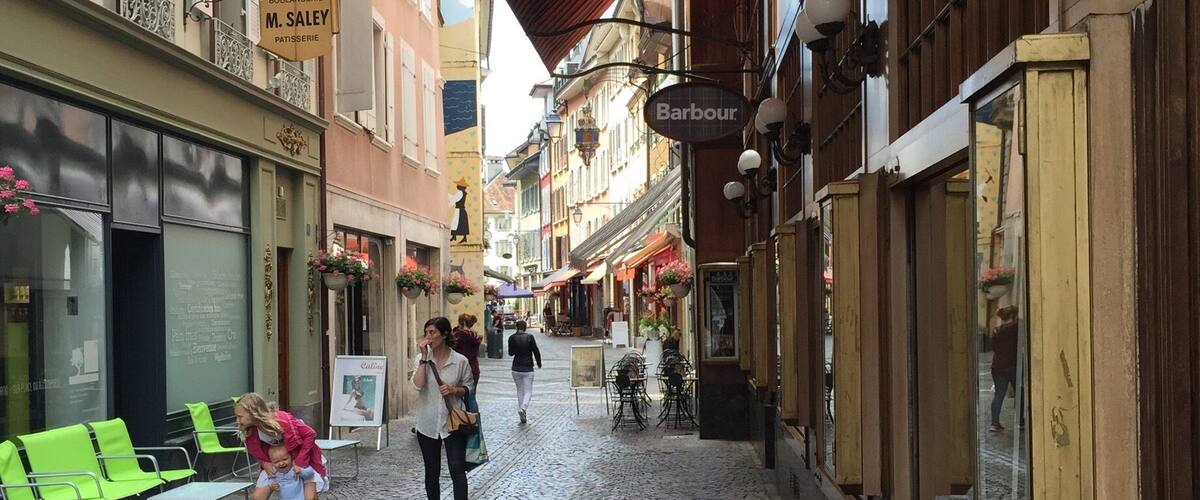 A cobblestone street with shops, a red awning, and hanging street lamps.