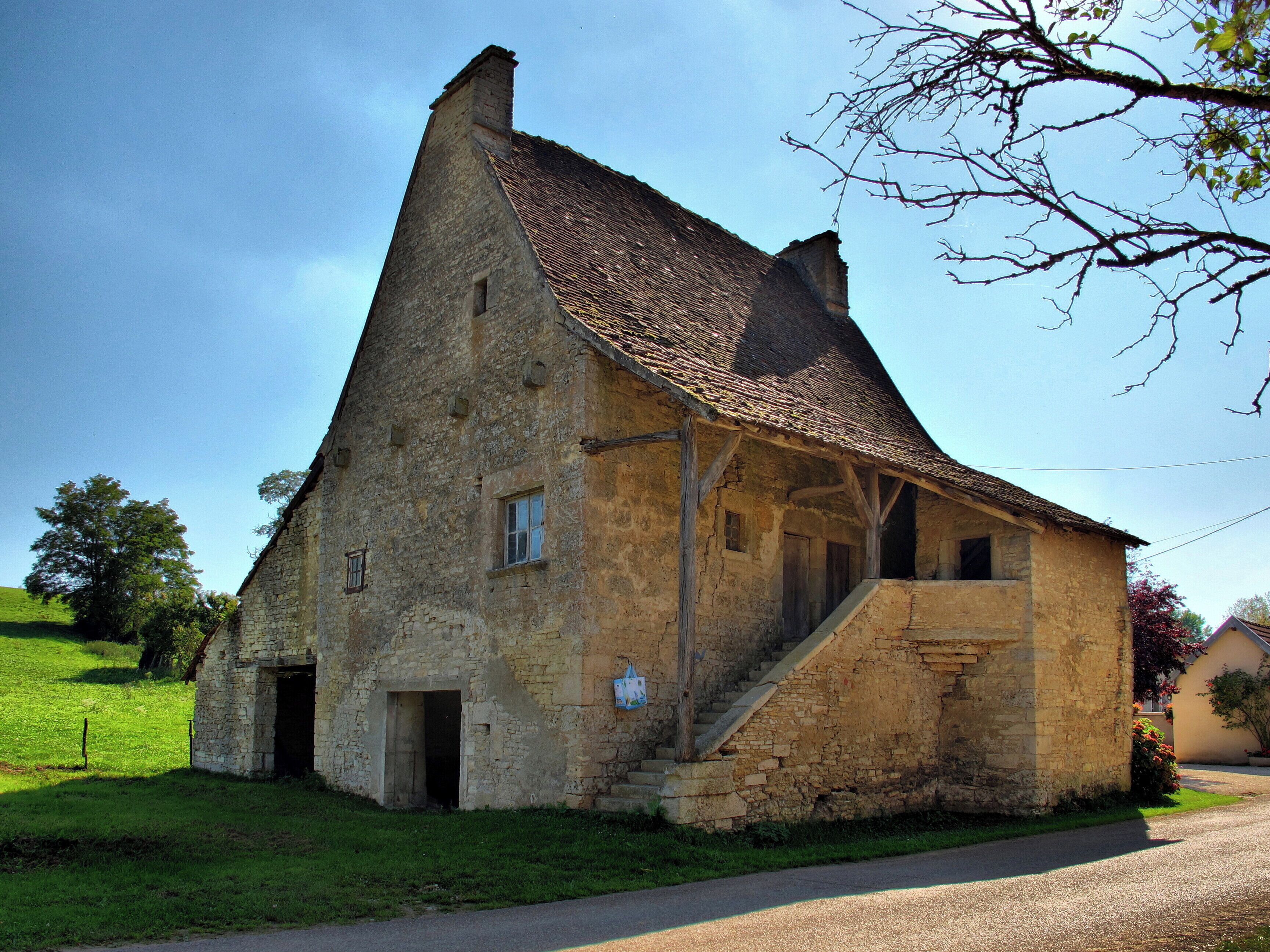 A stone building with a steeply pitched roof, a small staircase leading to the entrance, and a grassy field in the foreground.