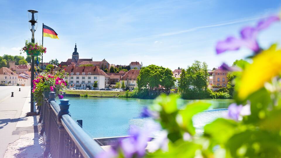 A riverside view with a bridge, buildings, and a flag.