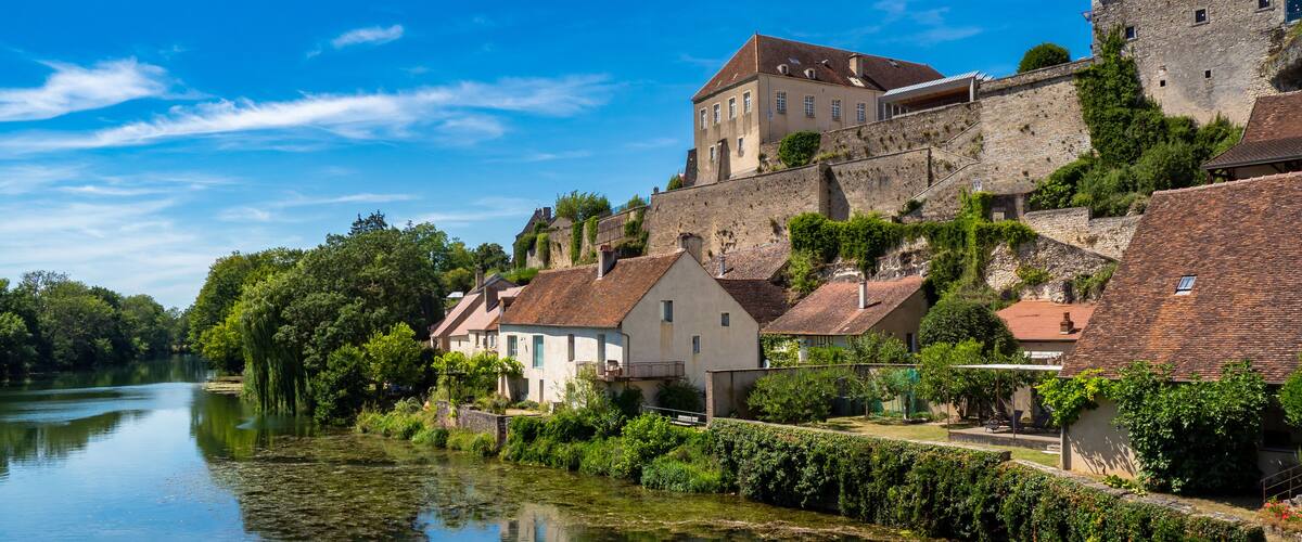 A river with houses and a castle on a hill.
