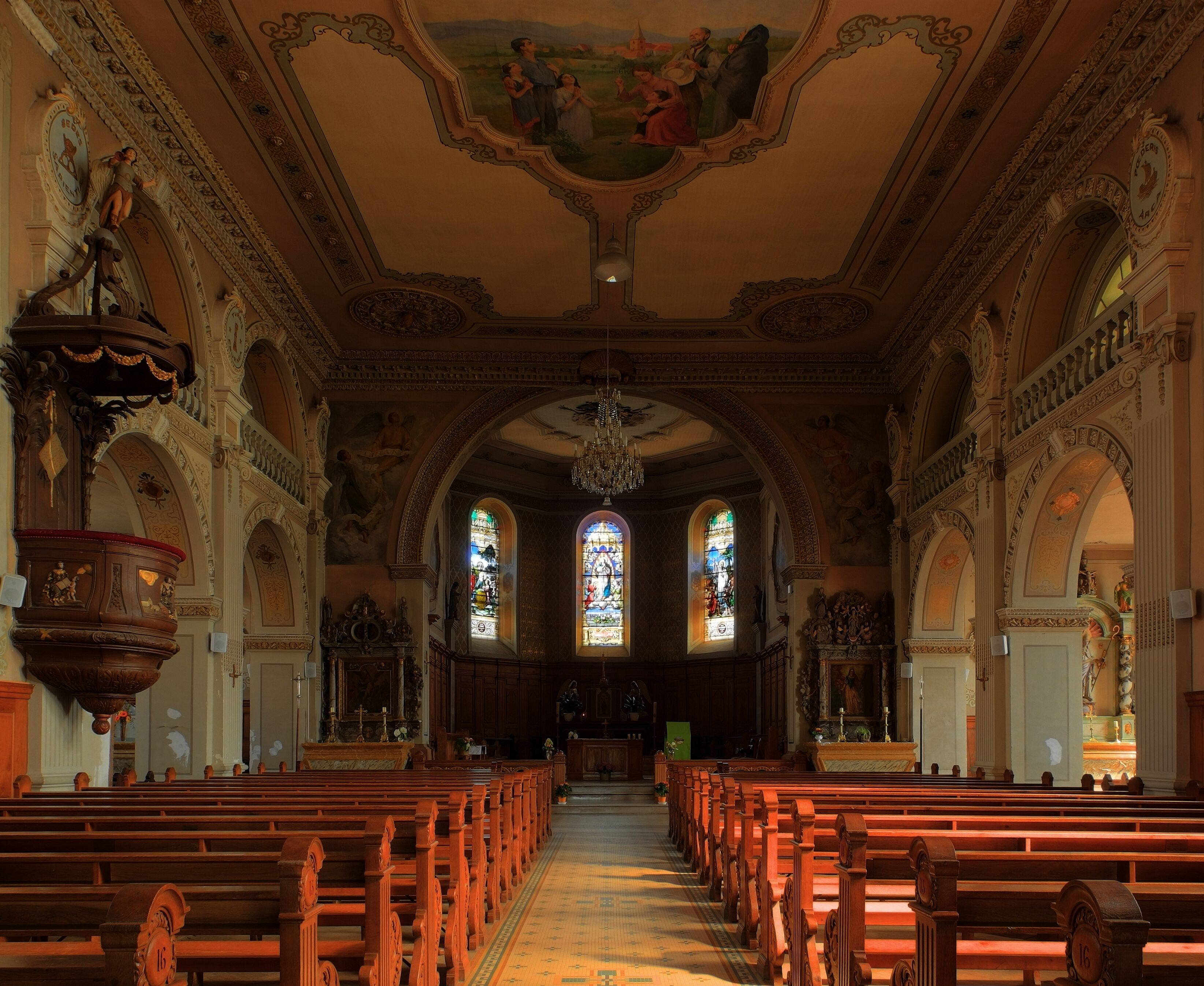 An ornate church interior with wooden pews, stained glass windows, and detailed ceiling artwork.