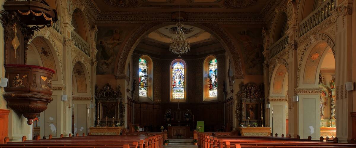 An ornate church interior with wooden pews, stained glass windows, and detailed ceiling artwork.