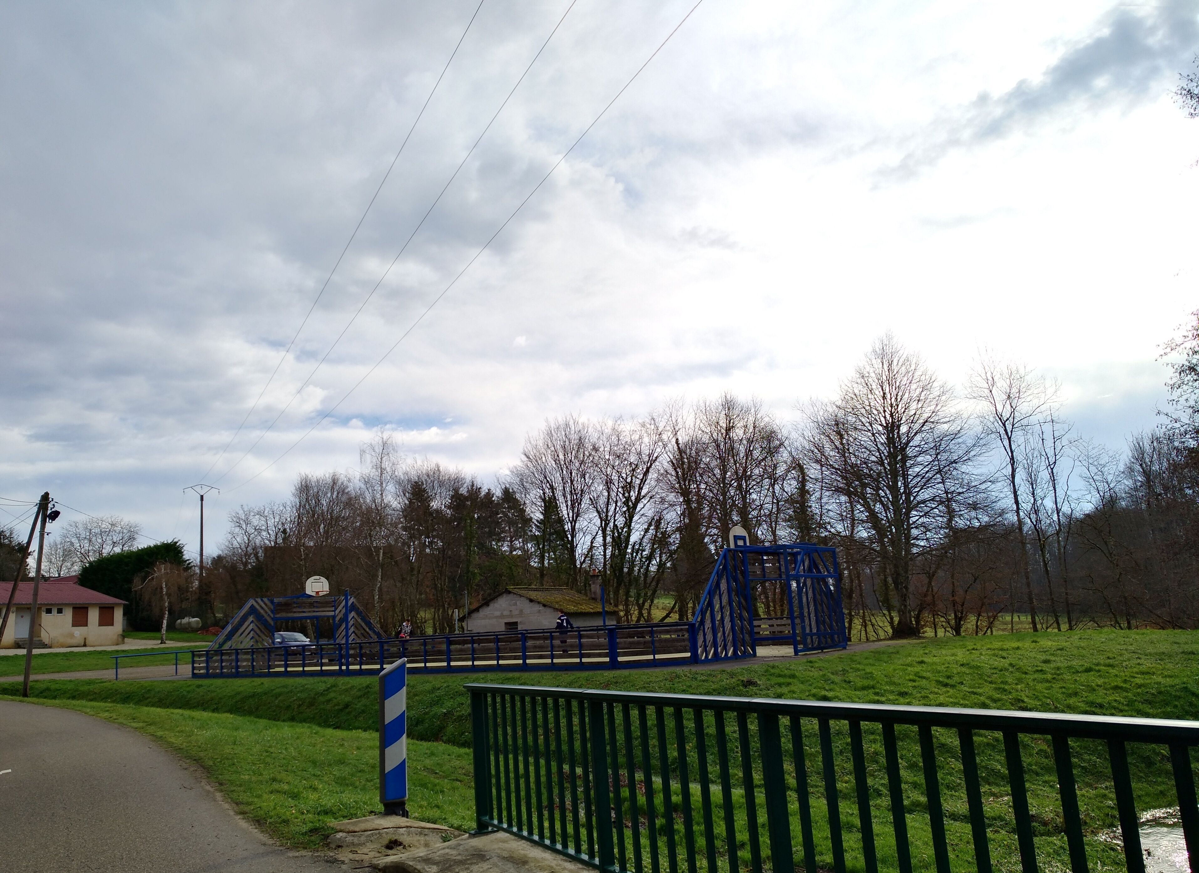 A park with a basketball court, a blue playground structure, and a green field.