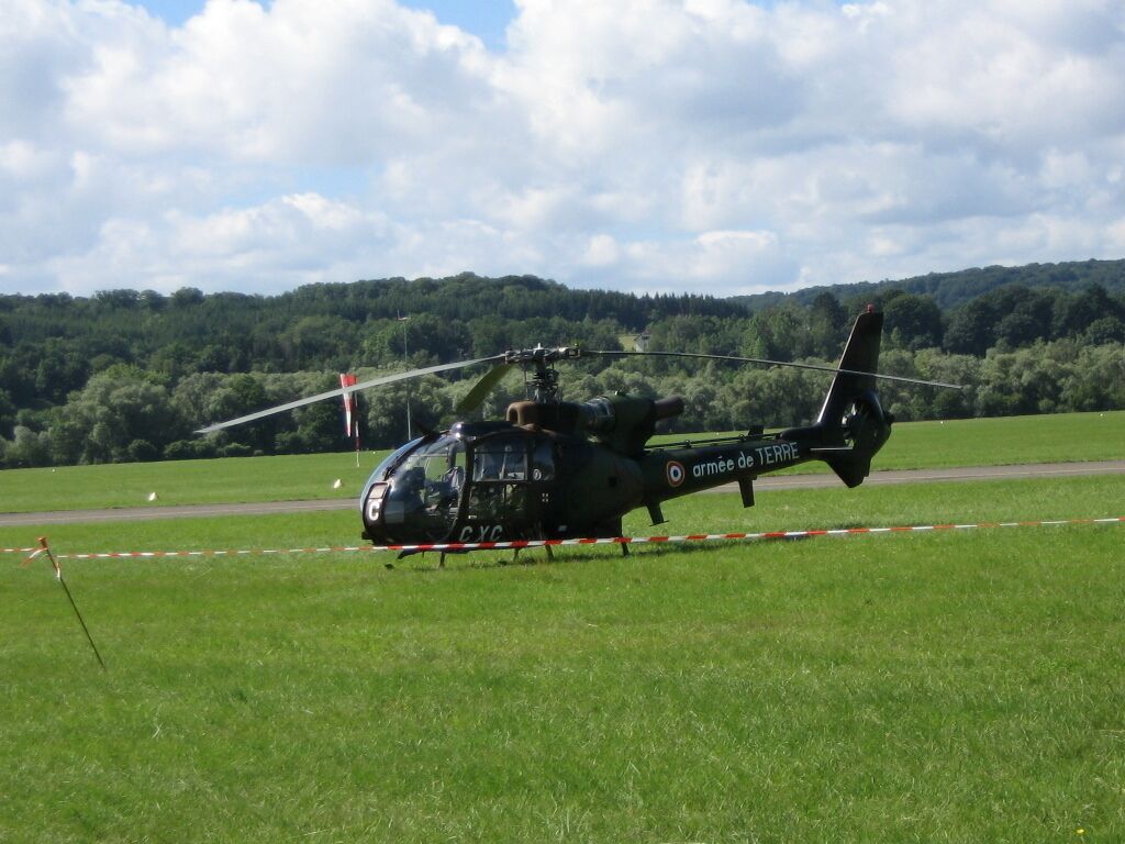 A black helicopter with "armée de terre" on its side parked on a grassy field with a forested hill in the background.