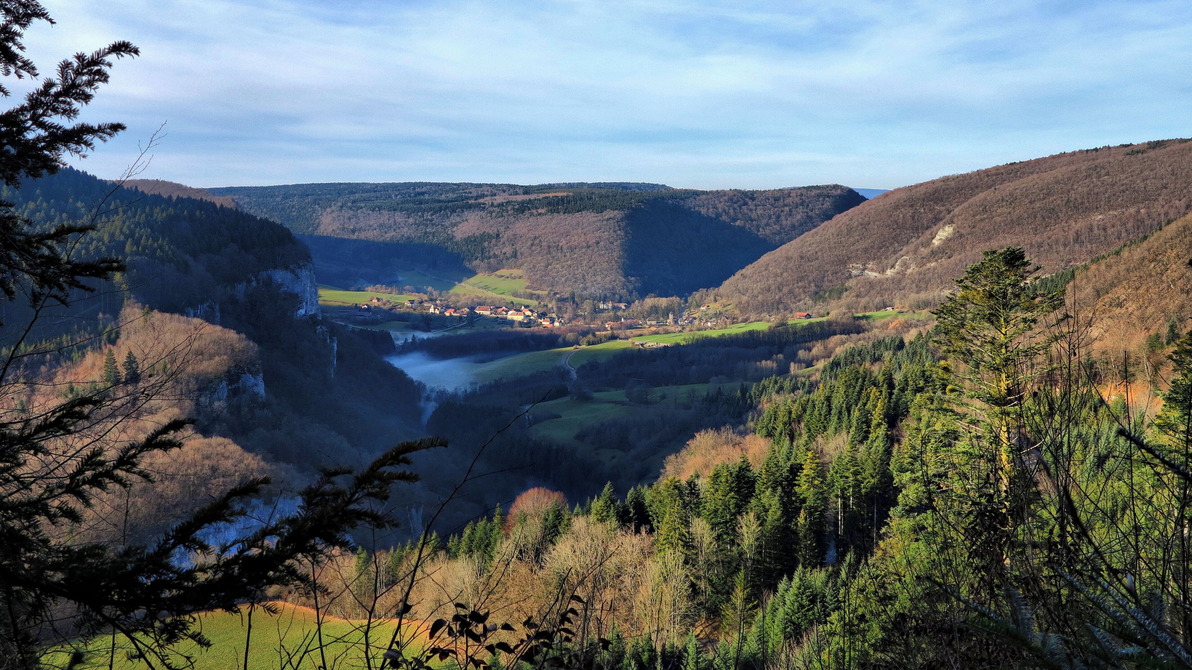 A valley with a river, surrounded by forested hills and a small town.