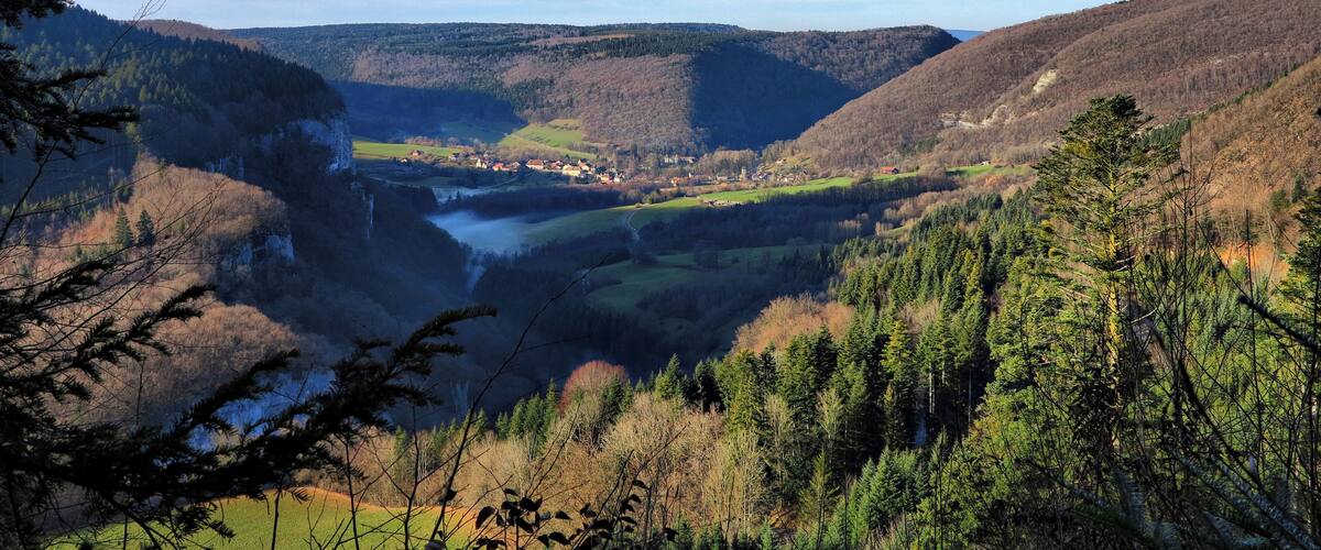 A valley with a river, surrounded by forested hills and a small town.