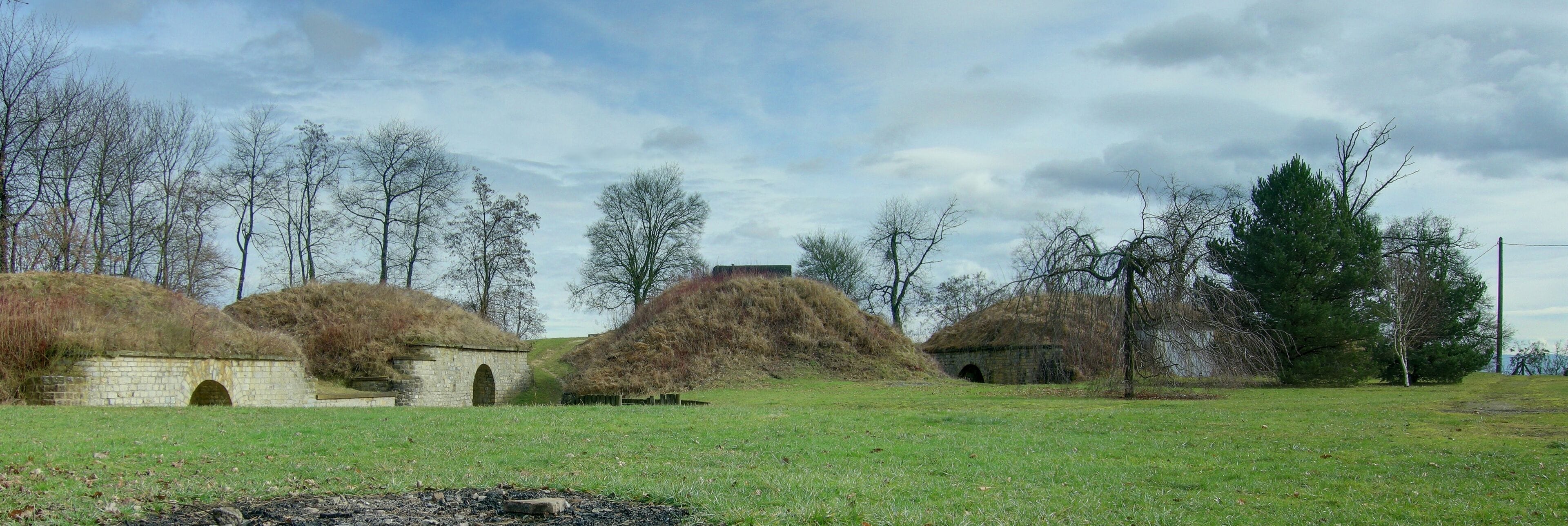 A grassy field with several stone huts and a stone bridge.