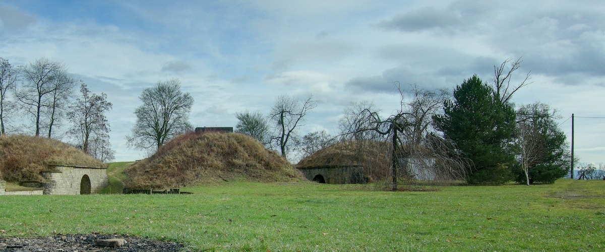 A grassy field with several stone huts and a stone bridge.