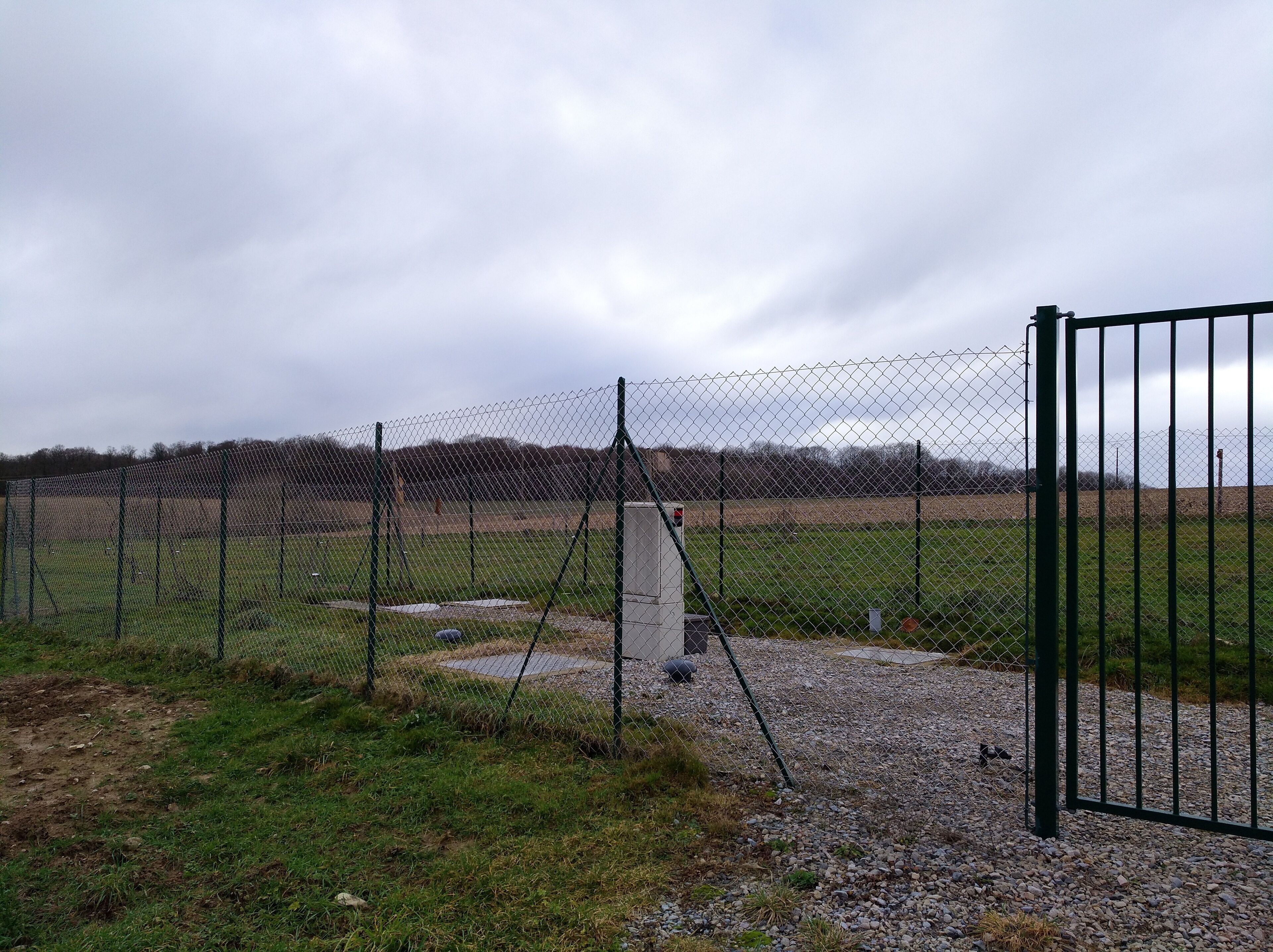 A fenced field with a gravel path and a metal gate.