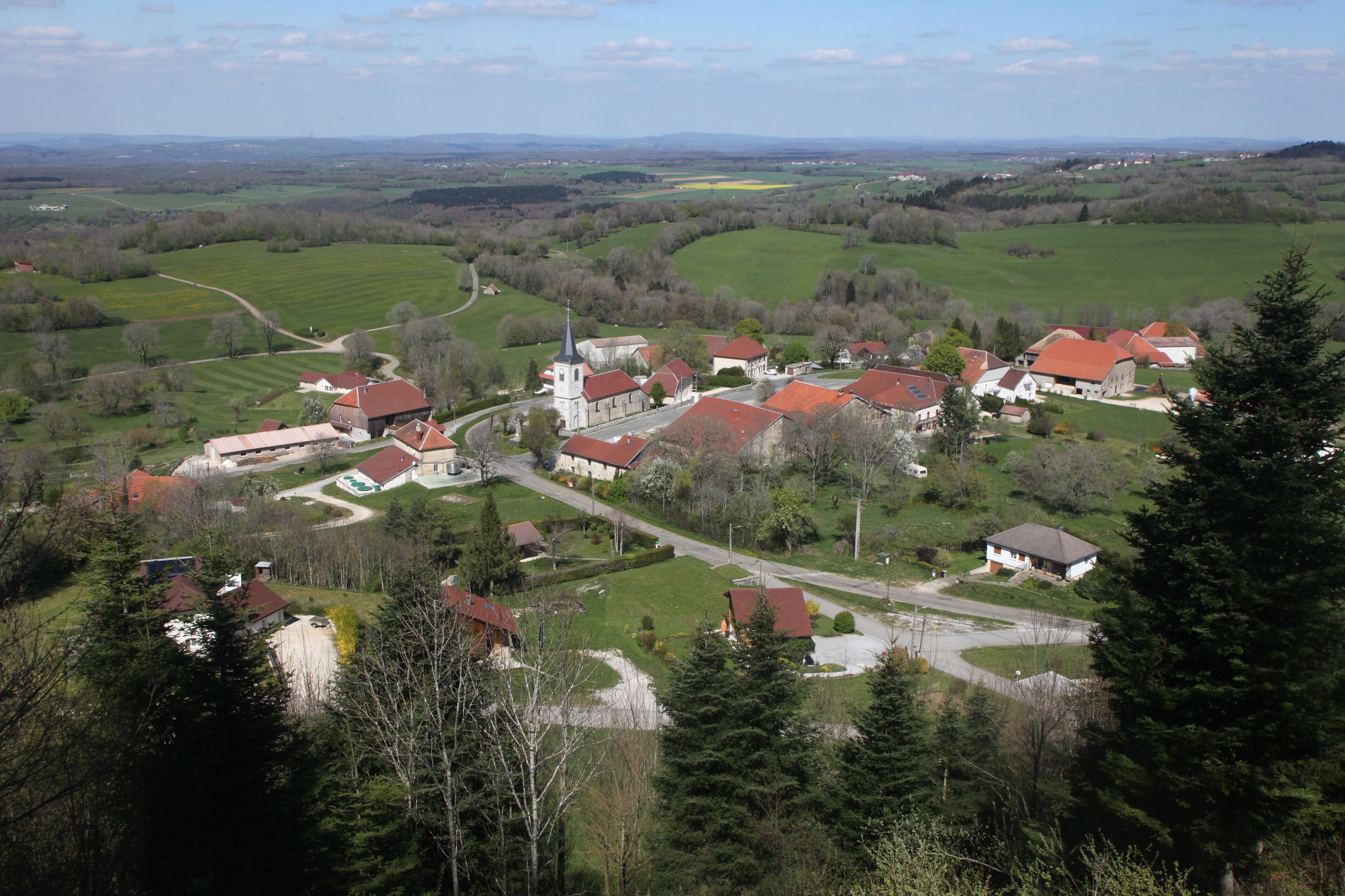 A rural village with red-roofed houses, a church, and surrounding green fields.