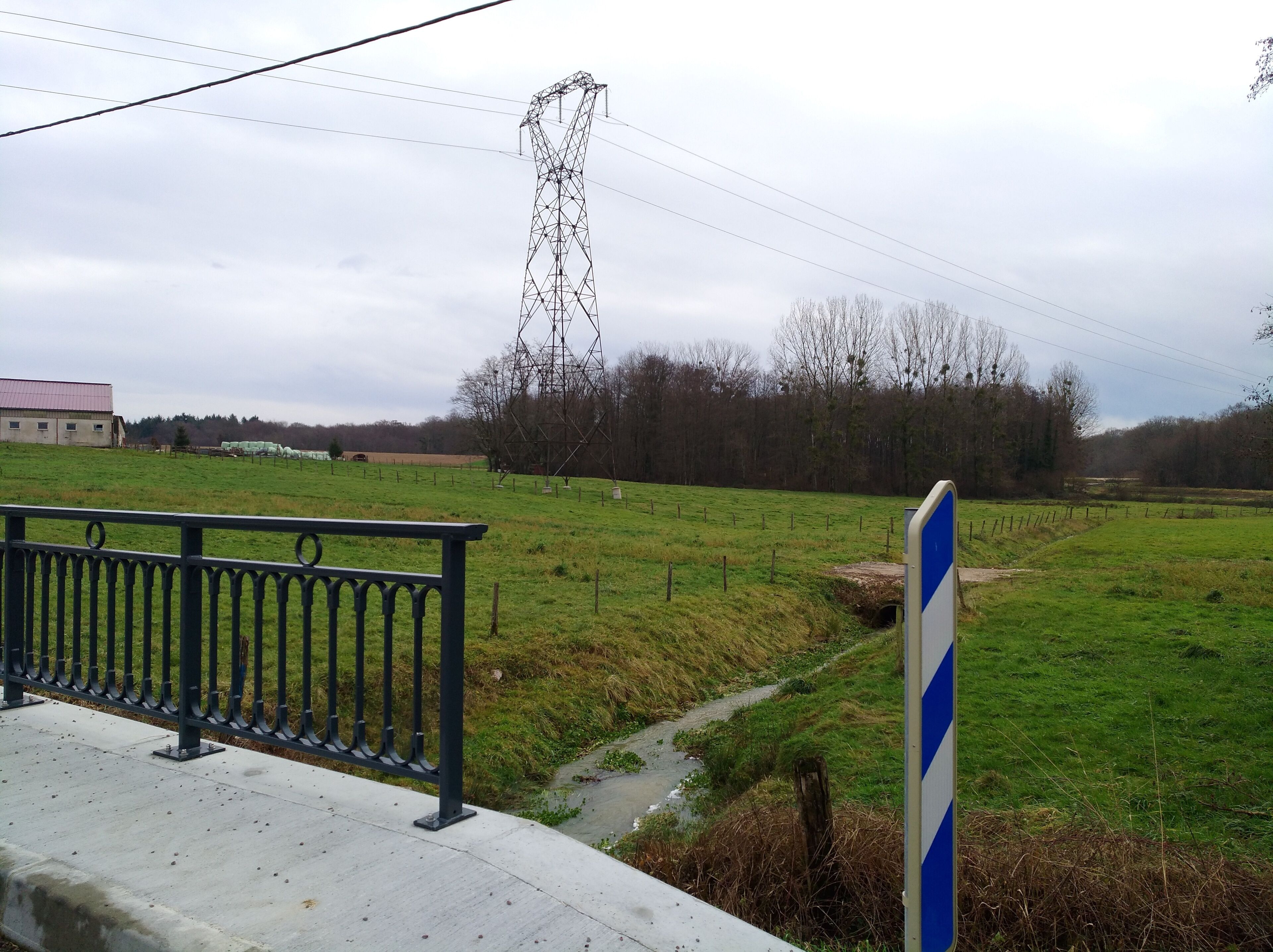 A rural landscape with a power line tower, a fenced field, and a building in the background.