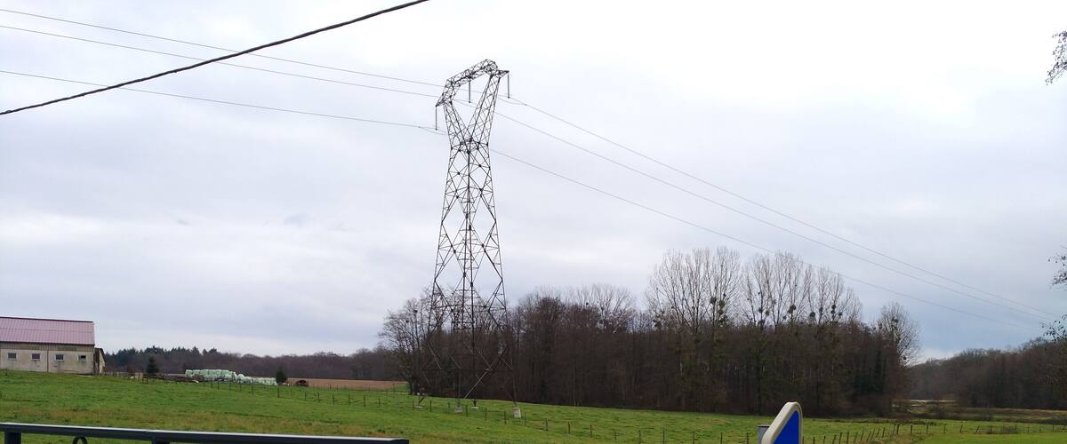 A rural landscape with a power line tower, a fenced field, and a building in the background.