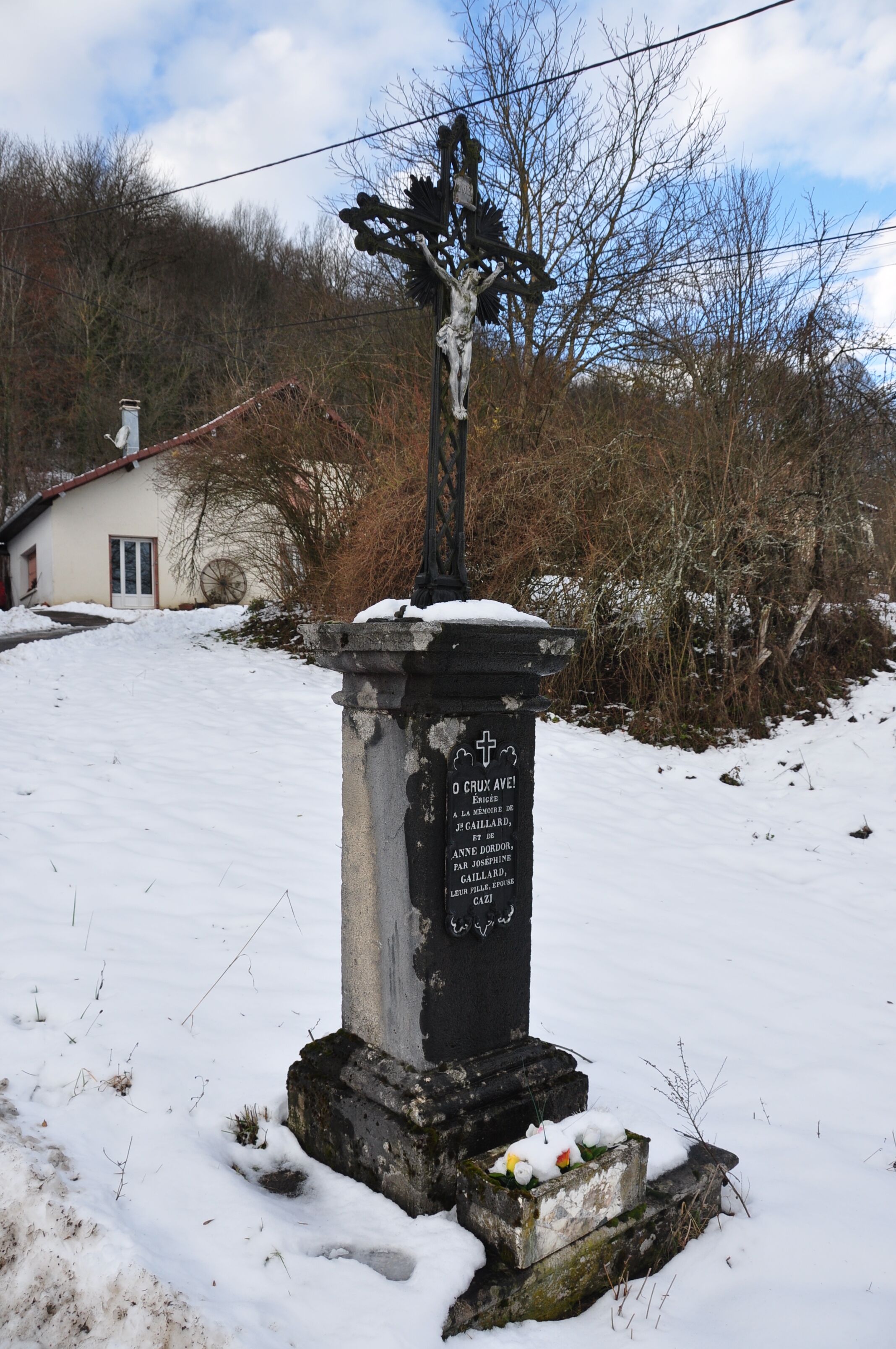 A gravestone with inscriptions in a rural setting with a house in the background.
