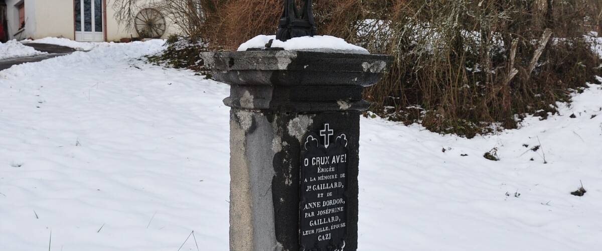 A gravestone with inscriptions in a rural setting with a house in the background.