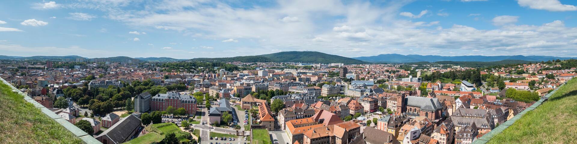 A panoramic view of a city with a river, surrounded by hills and mountains.