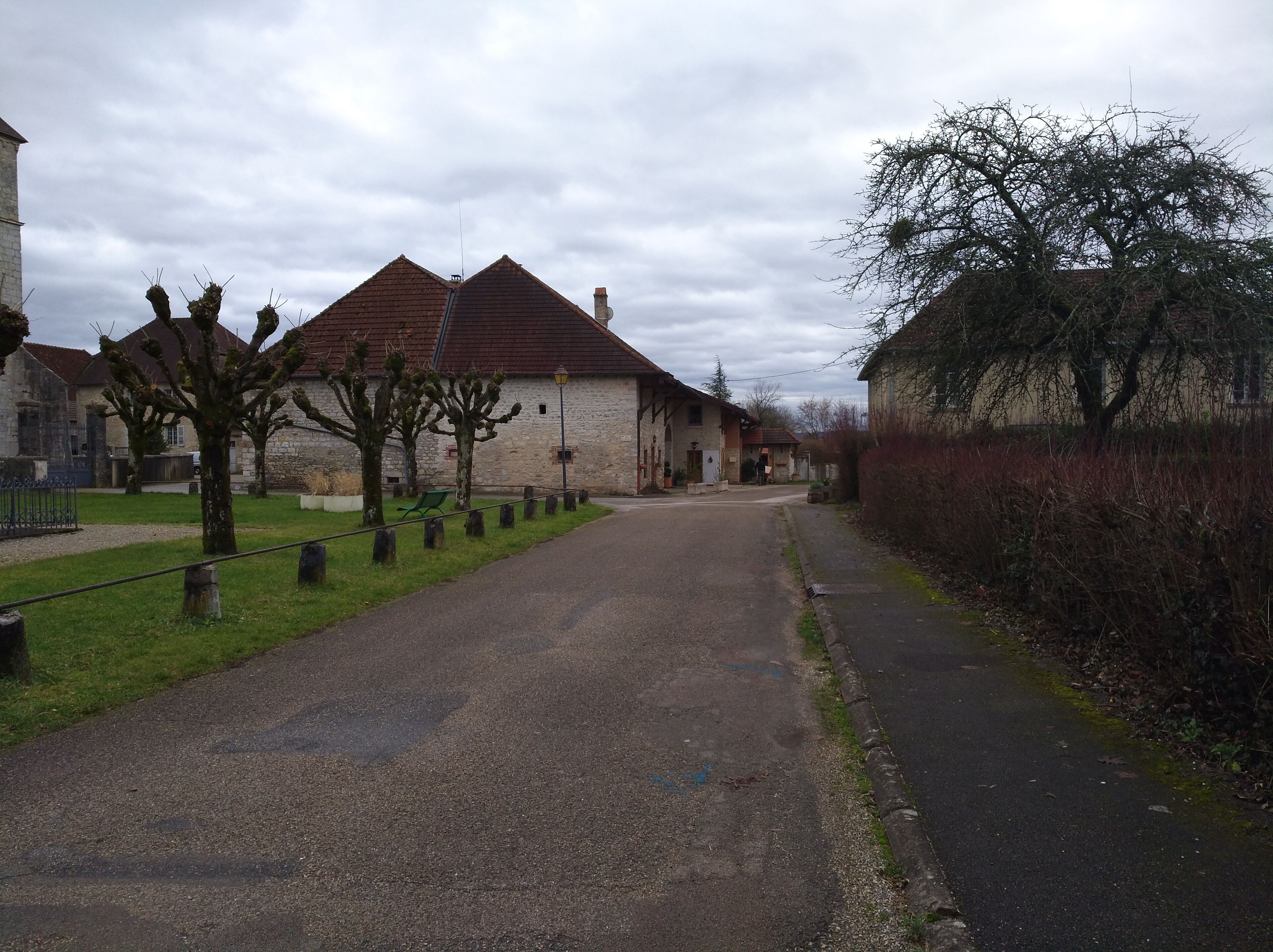 A quiet village street lined with stone houses and trees.