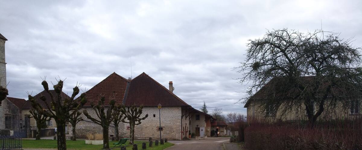 A quiet village street lined with stone houses and trees.