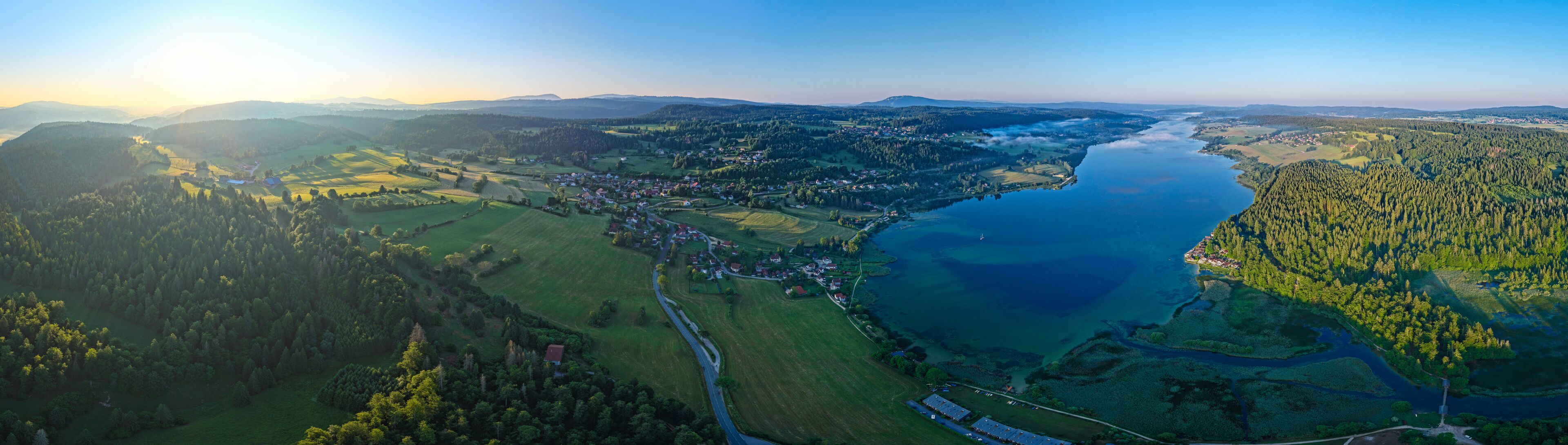 A river winding through a valley with a town on one side and forested hills on the other.